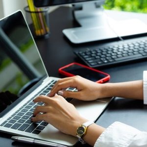 Close up hand of female typing on keyboard of laptop on table, working with technology device in modern office
